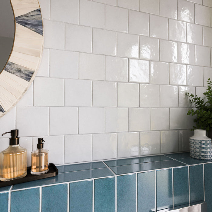 Zellige White Square 13.2cm x 13.2cm Moroccan style tiles, showcasing a softly irregular surface and glossy white finish that catches the light, paired with rich blue tiles and decorative accessories.